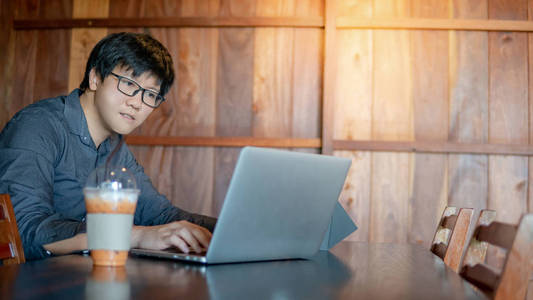 男亚洲商人戴着眼镜，在咖啡馆的木桌上用现代笔记本电脑工作。 在数字时代聪明工作。 物联网物联网概念