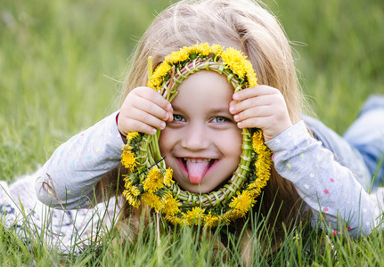 一个戴着蒲公英花圈的女孩躺在草地上。春天的概念