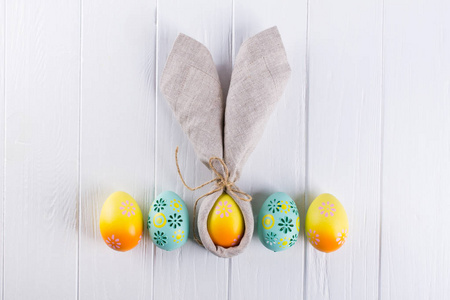 复活节假期背景与鸡蛋。 彩色彩绘的鸡卵放在一排兔子耳朵亚麻餐巾纸上