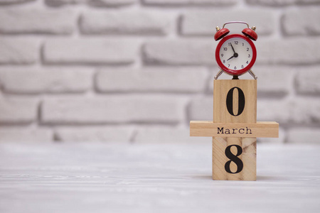 3月8日在木制日历上，白色砖块背景上有红色闹钟。 快乐的女人日。
