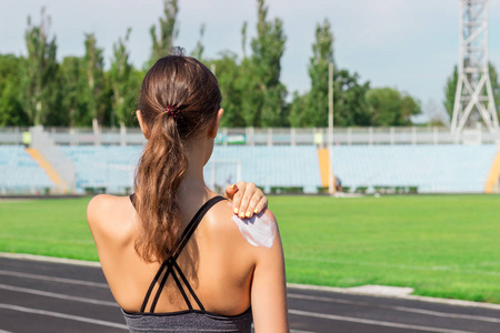 年轻的女跑步者站着，把防晒霜放在手上。 女孩在夏季早晨运动跑步前使用防晒霜。 运动和健康的概念。