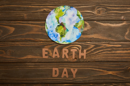 棕色木制背景地球日概念上的纸质字母和行星图片的顶部视图