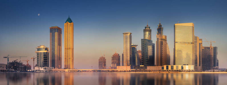 迪拜的城市景观和商业湾的全景，在阿联酋的早晨，摩天大楼在水面上反射。