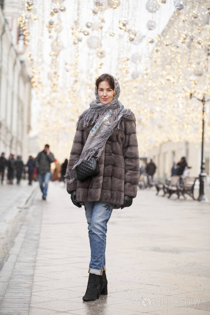 圣诞庭院中央穿着毛皮貂皮大衣和围巾的美丽黑发女人