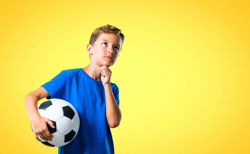男孩踢足球，思考黄色背景