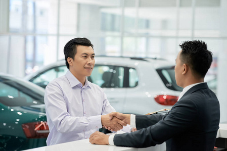 微笑的推销员和顾客握手在汽车陈列室