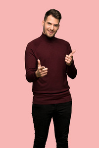 穿着高领毛衣的男人指着前面，在粉红色的背景上微笑