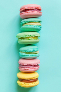 甜杏仁五颜六色，粉红色，蓝色，黄色，绿色，通心粉或马卡龙甜点蛋糕孤立在时尚的蓝色粉彩背景上。 法式甜饼。 最低食品烘焙概念。 平