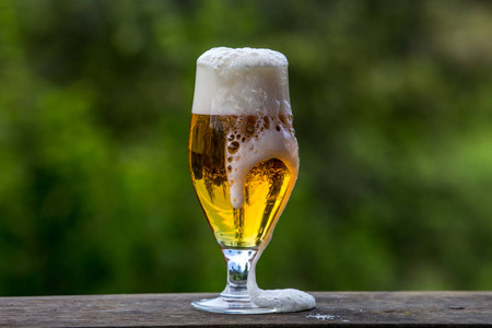 绿色自然背景木桌上有泡沫和气泡的淡啤酒。 啤酒是一种酒精饮料，由酵母发酵麦芽制成，带有啤酒花的味道