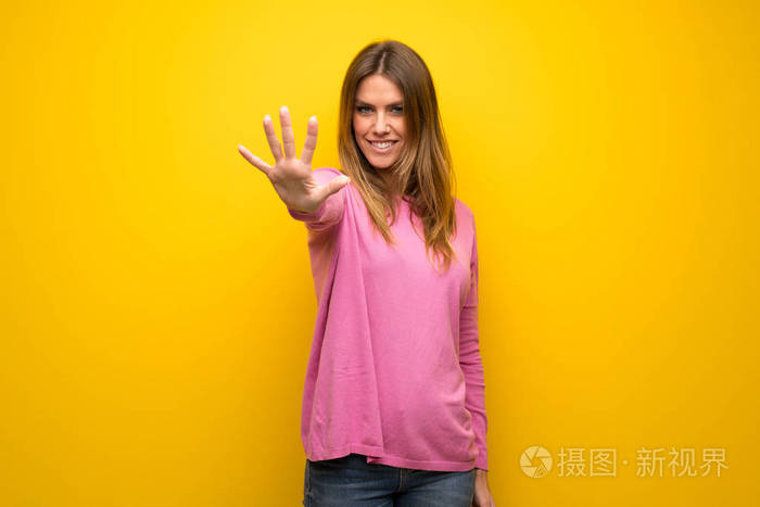 女人穿着粉红色的毛衣在黄色的墙上数着五个手指