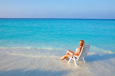 年轻漂亮的女人晒黑的沙滩椅，它放在海洋中