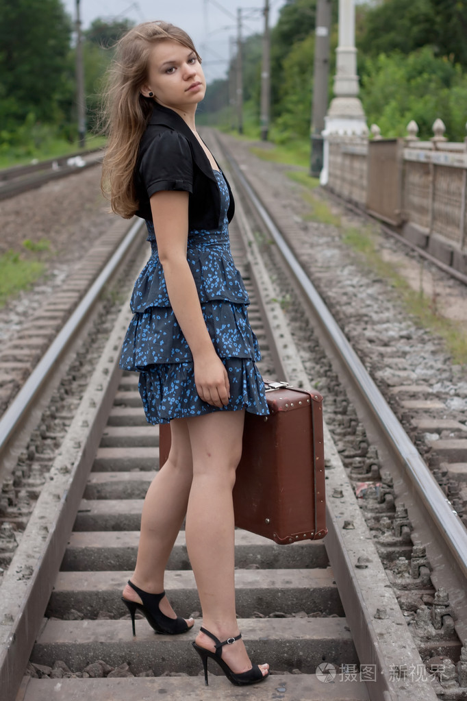 一个行李箱站在铁轨上的女孩