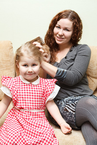 母亲和小女儿坐在沙发上。女人梳的女儿头发