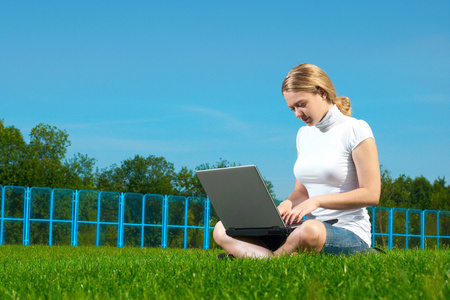 与绿色的草坪上的笔记本电脑女孩