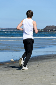 运动年轻男性在海滩上运行。从背面