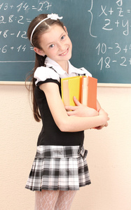 漂亮的小女孩穿着校服与教室里的书