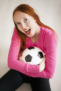 吸引人的金发女孩拿着一个足球球和坐在地板上