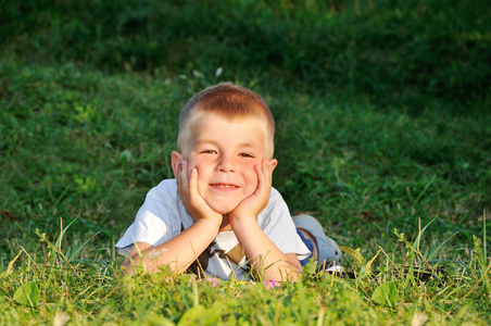 快乐的小男孩躺在草地上，看看相机的性质