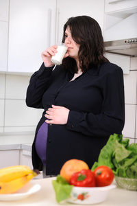 怀孕的女人在厨房里喝牛奶