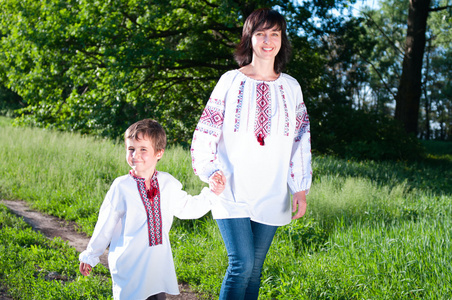 母亲和儿子在传统乌克兰衬衫走在草地上