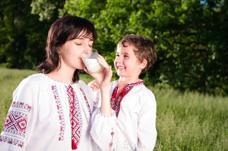 母亲和儿子在传统乌克兰衬衫喝牛奶户外