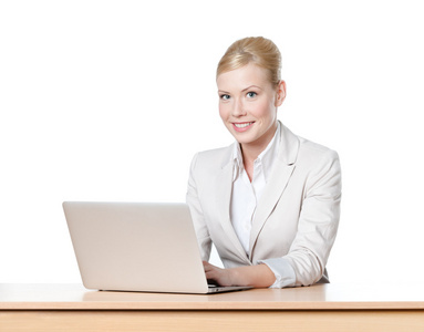 年轻女商人坐在办公室的桌子上用的笔记本电脑，笑脸。