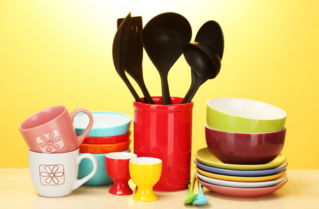 明亮的空碗 杯子和厨房用具在黄色背景上的木桌上