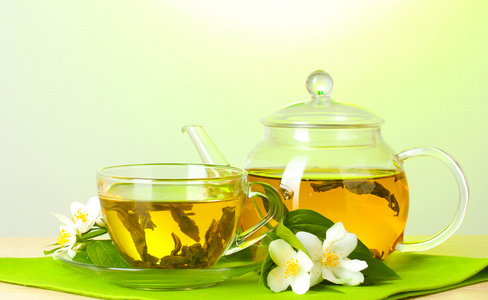 绿茶与茉莉花在杯子和绿色背景上的木桌上的茶壶