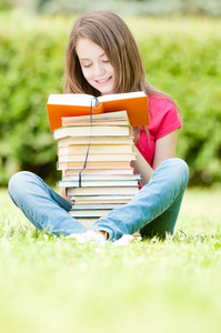 快乐的学生女孩坐在草地上和阅读