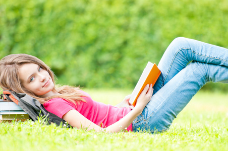 快乐的学生女孩躺在草地上，已打开的书