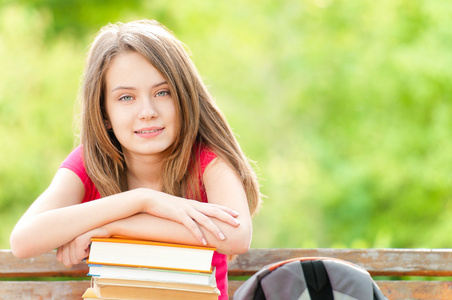 快乐的学生女孩坐在长椅上与书和微笑