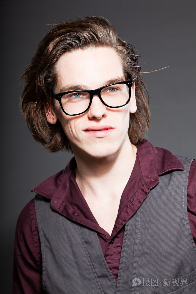 英俊的年轻男子灰色背景上孤立的棕色长头发.戴着黑色复古眼镜.