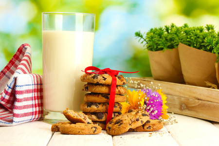 一杯牛奶，巧克力芯片与红丝带和野花的 cookie 在绿色背景上的木桌上