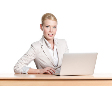 年轻商业女人坐在办公室的桌子上用的笔记本电脑，笑脸。