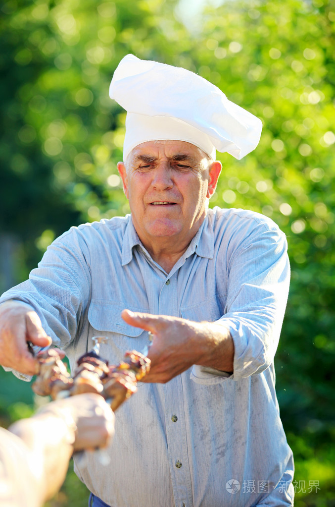 成熟的白种男人在举行烤的羊肉串的厨师的帽子