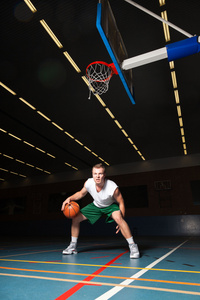 坚强健康的年轻人在健身房室内打篮球。身穿白衬衫和绿色短裤