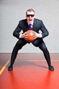 愤怒的业务人打篮球。戴着墨镜。很帅与短的金发的年轻人。室内体育馆