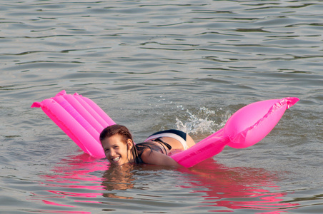 可爱少女躺在粉红色的床垫上，漂浮在海面上