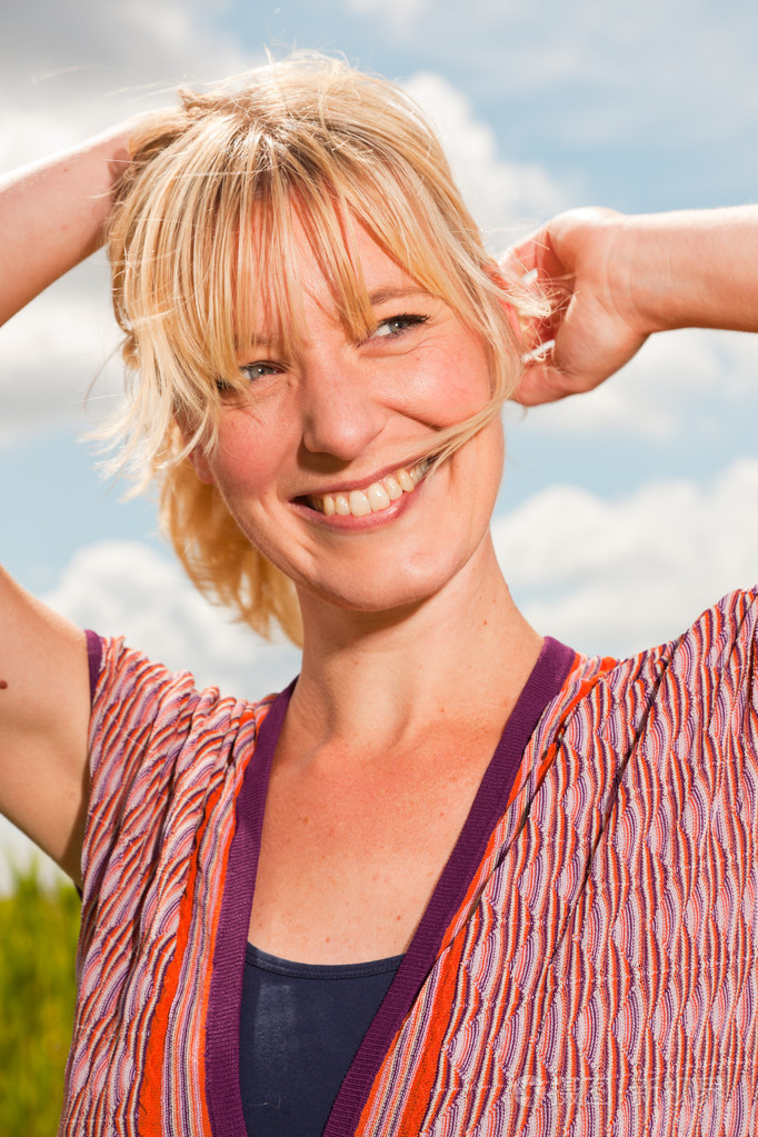 享受自然的快乐年轻漂亮金发女郎具有高草的字段蓝多云的天空穿红色