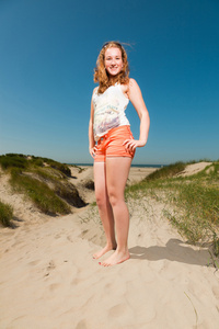 快乐有热的夏天一天享受海滩附近沙丘的红色的长头发的漂亮女孩。清澈的天空