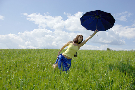 美丽的女人在绿草的字段和云天空中持有蓝伞