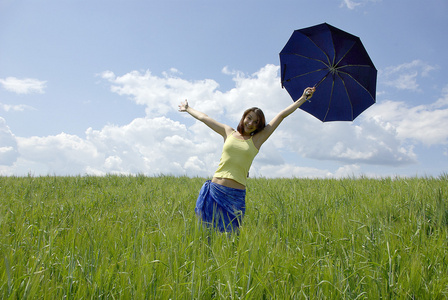 美丽的女人在绿草的字段和云天空中持有蓝伞