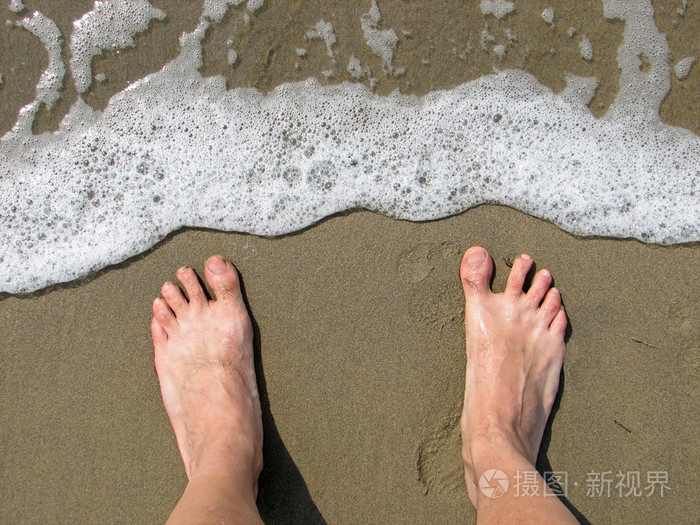 两个裸脚在沙滩上等待波