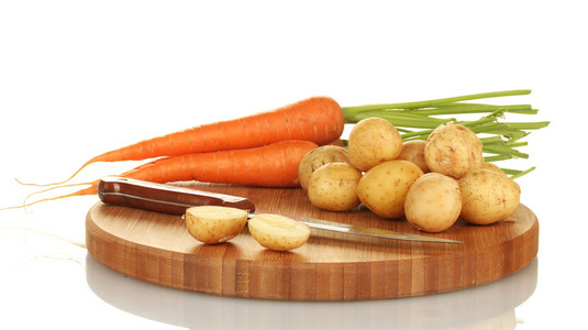 年轻的土豆和胡萝卜在一个切割板上用刀上白色隔离