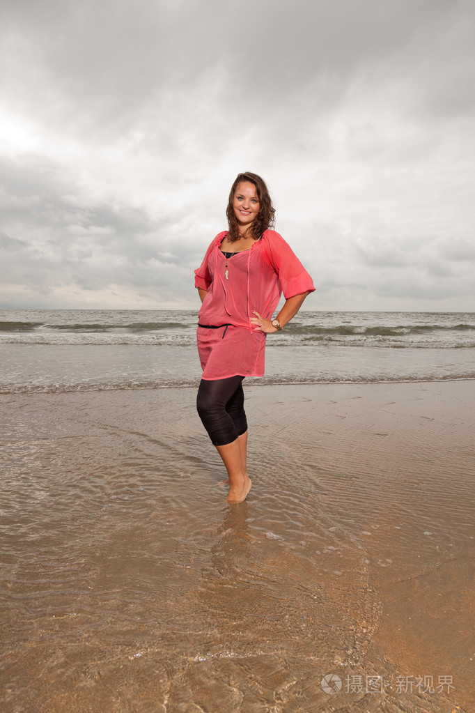 快乐的年轻女人享受海滩附近的户外自然站在水中棕色的头发身穿粉红色