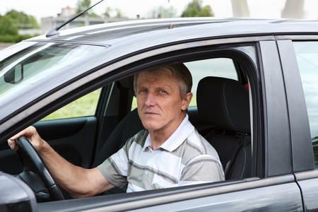 成熟的男人坐在车上驾驶员座位和持有方向盘