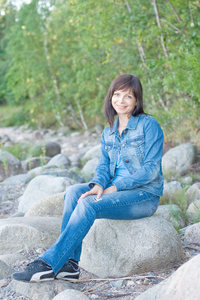 坐在湖边的一块岩石上的漂亮女人