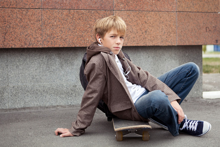 学校青年坐在学校附近的滑板上