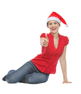 圣诞帽子坐在地板上，显示的拇指的幸福女人