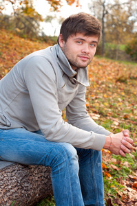 快乐年轻男子坐在秋天公园户外肖像
